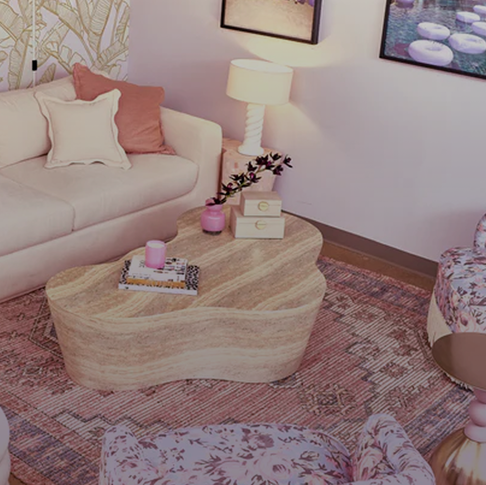 A heart-shaped wooden coffee table styled in a cozy living room setting with a cream sofa, patterned pillows, a floral rug, and a matching floral armchair.